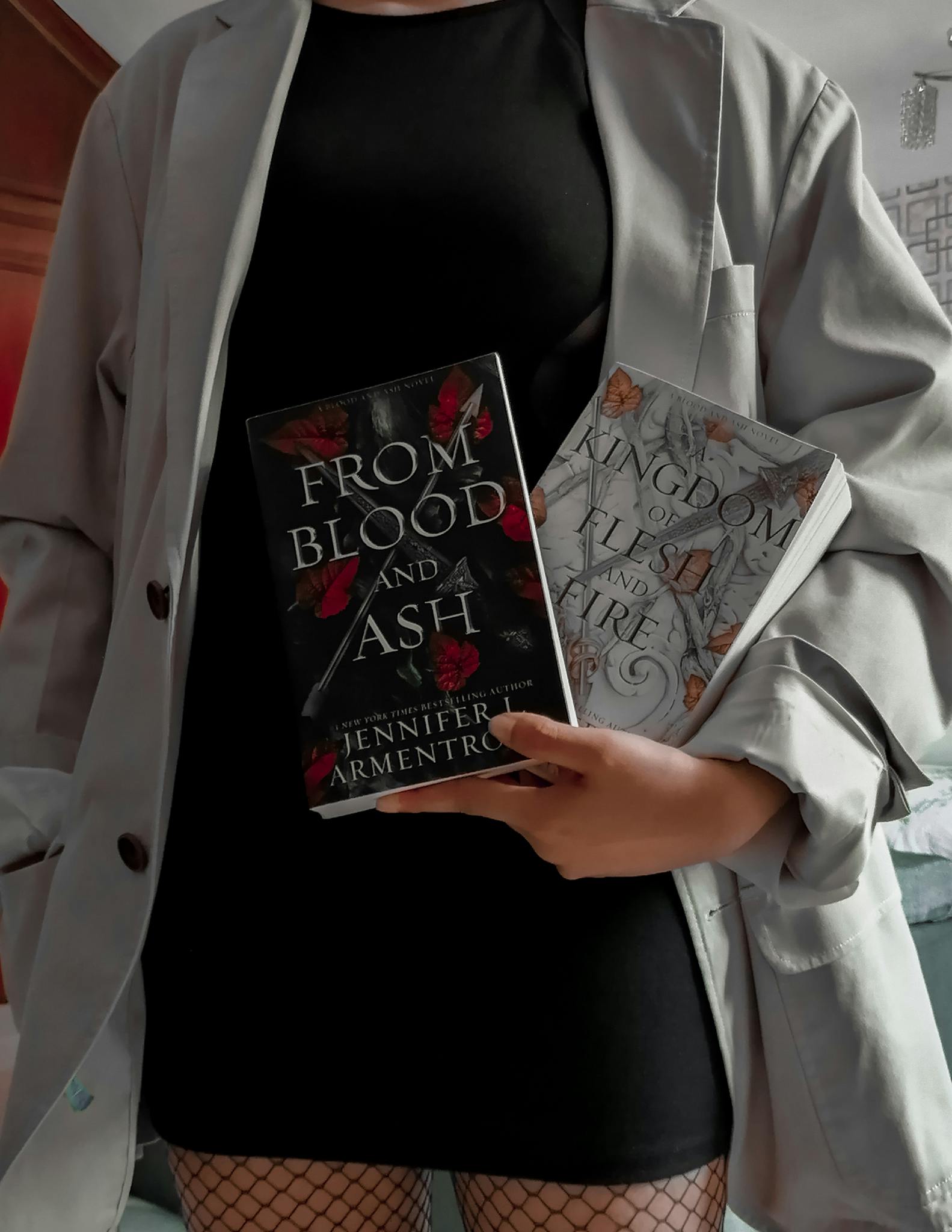 A woman in a chic outfit holds two popular fantasy novels indoors.