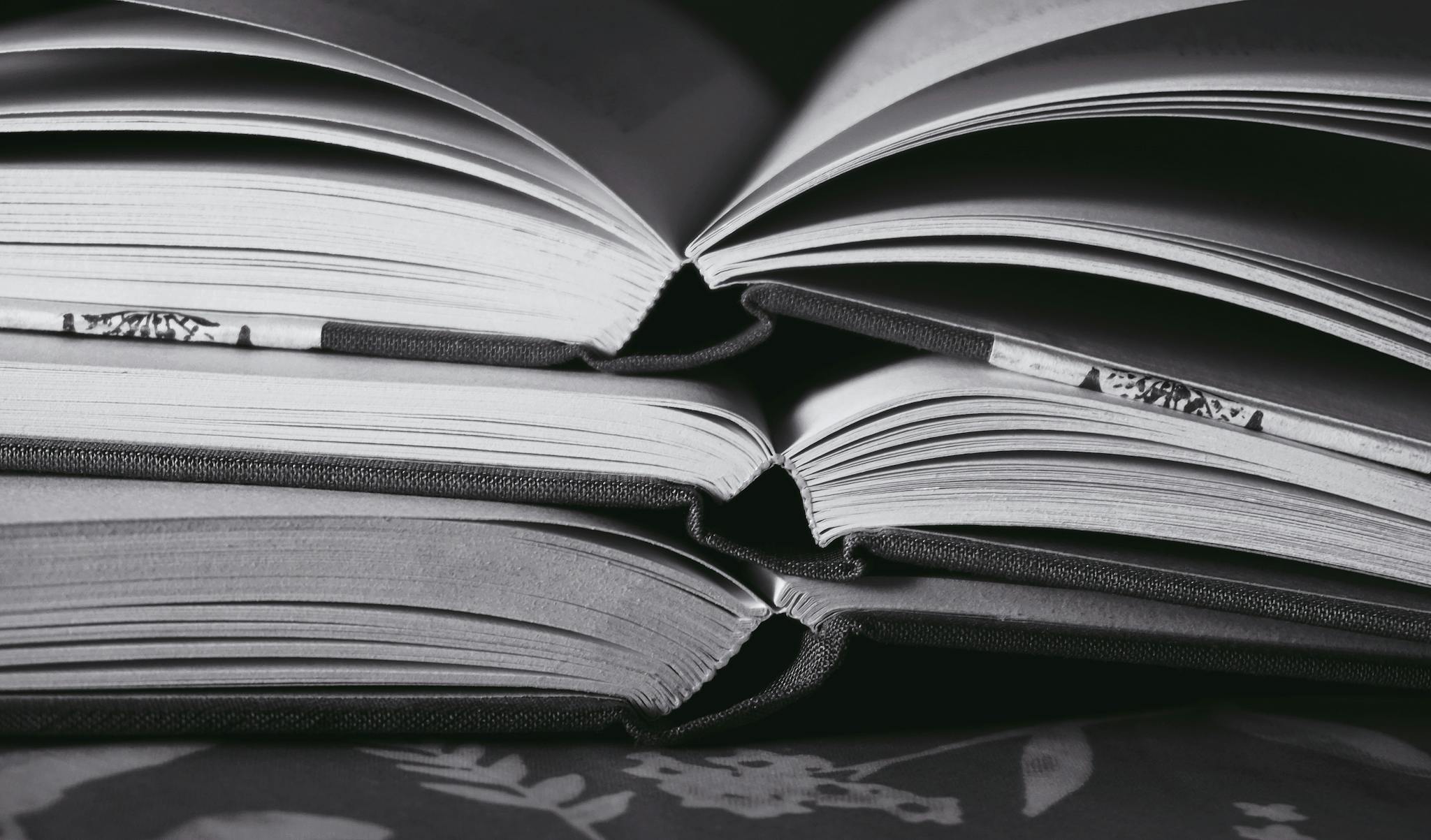 Artistic monochrome image of stacked open books, highlighting their pages and textures.